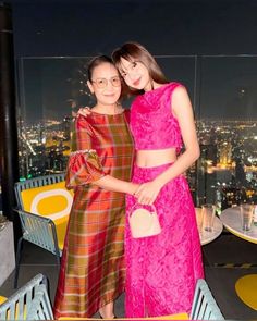 two women standing next to each other in front of a cityscape at night