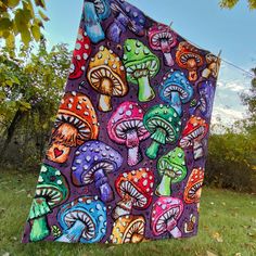 a blanket with colorful mushrooms on it is hanging in the grass near some trees and bushes