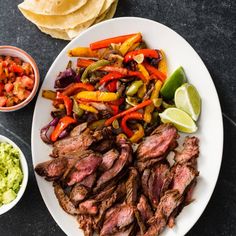 a white plate topped with steak and vegetables next to guacamole, tortilla chips and salsa