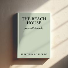 the beach house guest book sits on a white wall next to a window with light coming through it