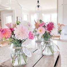 three vases filled with flowers sitting on top of a wooden table in a kitchen