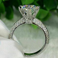 a close up view of a diamond ring on a white cloth with greenery in the background