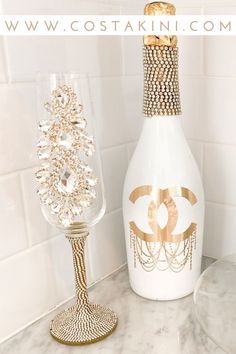 a white bottle with gold decoration next to a wine glass on a marble counter top