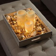 two candles are lit in a box with ornaments around it on a couch that is decorated with gold and white balls