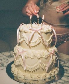 a woman lighting candles on top of a cake that is decorated with white ruffles and pink bows