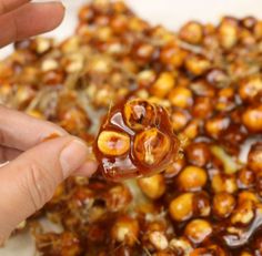 a person holding a spoon full of caramel coated nuts with chocolate on top, in front of a pile of other candies