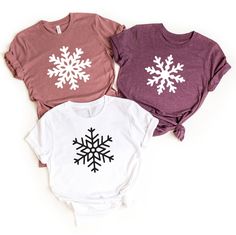 three t - shirts with snowflakes on them are sitting next to each other