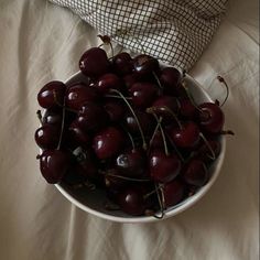 a white bowl filled with cherries on top of a bed