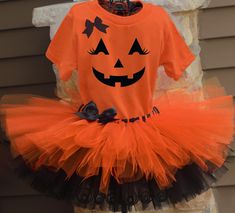 an orange shirt with a black bow and a pumpkin tutu is on display in front of a house