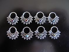 six pairs of silver colored metal rings on a black surface, with beads and stones in the middle