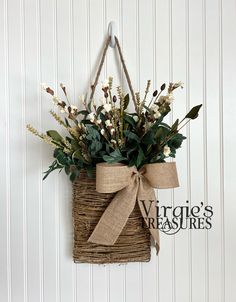 a wicker basket hanging on the wall with flowers and greenery tied to it