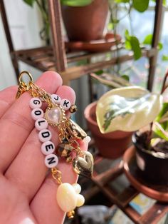 a person holding a keychain with letters and charms on it in front of a potted plant