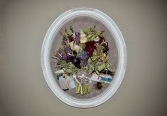 an arrangement of flowers in a white circular frame on the wall above a toilet paper dispenser