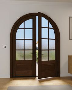 an open wooden door with two arched glass panes on the inside of it, in front of a white wall and wood floor