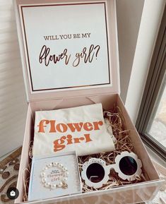 an open box containing sunglasses, jewelry and a flower girl t - shirt that says will you be my flower girl?