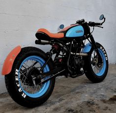 an orange and blue motorcycle parked next to a white wall