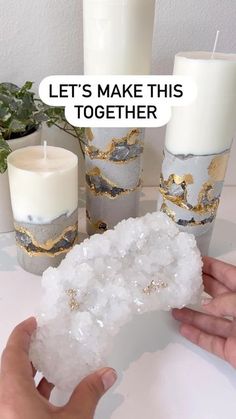 a person holding a piece of white rock next to some candles and plants on a table