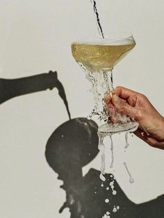 a person holding a wine glass in front of a wall with the shadow of a man's head on it