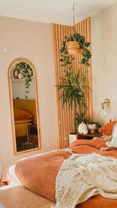 a bed with an orange comforter in a bedroom next to a mirror and potted plant