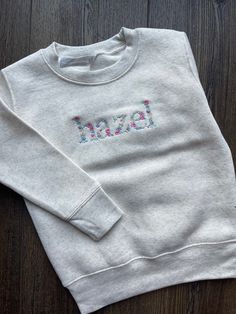 Choose from heather grey, navy, pink, black or royal. Each sweatshirt is made from 60% cotton and 40% polyester. Each sweatshirt is embroidered with the word of your choice using the floral alphabet shown. Sweatshirts fit true to size Please wash on cold and dry on low. In the notes to seller please enter the word you would like EXACTLY as you would like it Winter Crew Neck Sweater With Letter Embroidery, Heather Crew Neck Sweatshirt For Loungewear, Heather Crew Neck Spring Sweater, Heather Grey Fleece Crew Neck Tops, Embroidered Long Sleeve Tops For Loungewear, Long Sleeve Embroidered Sweater For Loungewear, Heather Grey Long Sleeve Cotton Sweatshirt, Heather Grey Cotton Sweater For Fall, Casual Heather Cotton Sweater