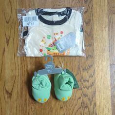 a pair of baby shoes sitting on top of a wooden floor next to a t - shirt