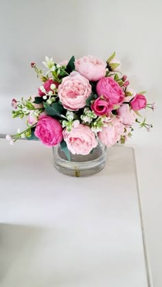 a vase filled with pink flowers sitting on top of a white table next to a wall