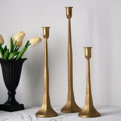 three gold candlesticks and one black vase with tulips