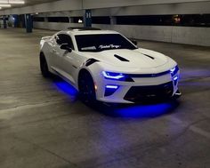 a white chevrolet camaro with blue lights on it's hood in a parking garage