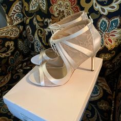 a pair of white high heeled shoes sitting on top of a box in front of a couch