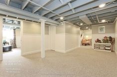 an empty living room with white walls and ceiling beams, carpeted flooring and storage bins