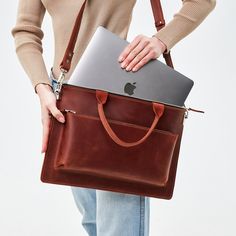 a woman holding an apple laptop in her brown leather bag, with the lid open