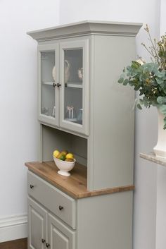 a white vase filled with flowers sitting on top of a wooden table next to a gray china cabinet