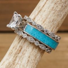 two wedding rings with turquoise stones and diamonds on each band, sitting on a piece of driftwood