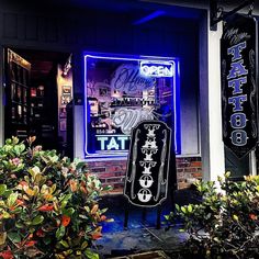 an outside view of a tattoo shop with neon signs and flowers in the foreground