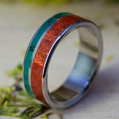 a wedding ring with wood inlays and green enamel inside the band, sitting on a table