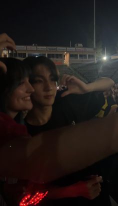 two people are taking pictures with their cell phones at a baseball game in the dark