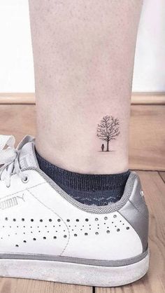 a small tree tattoo on the ankle is shown in black and grey colors, with an arrow