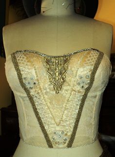 "Vintage bustier adorned for a wedding evening or honeymoon. This is adorned with various antique textiles and trims dating from the Turn of the Century to the 1920s. Cream lace with a \"V\" shaped center. Rhinestone trim embellishes the top part of the bustier with a 1900's metallic applique. Remnants of a 1920s silk wedding dress is encrusted throughout the front panel and features a white beaded lattice design with flower petals detailed with more rhinestones. This would be ideal for a vintag Luxury Evening Bustier Corset, Luxury Vintage Underbust Bodice, Victorian Wedding Corset With Historical Design, Victorian Corset With Historical Design For Wedding, White Victorian Wedding Corset, Glamorous Wedding Corset With Fitted Bodice, Fitted Bodice With Historical Design For Wedding, Glamorous Fitted Bodice For Wedding, Glamorous Wedding Corset With Sweetheart Neckline