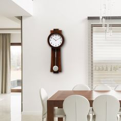 a clock mounted to the wall above a dining room table with white chairs and a chandelier