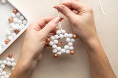 two hands are holding bead balls and stringing them to make an ornament