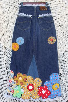 "Add some flower power flare to your day wearing this uniquely you skirt made from vintage jeans, showcasing a flower border made from vintage material, bright buttons, fabric yo-yos, and of course, lacey trim. Don't be caught without this flowering wonder of a skirt! Has a 6\" zipper and button closure. Size Small. Waist Size: 12\" across Length: 34 1/2\" Weight: 1 lb 12 oz." Vintage Floral Embroidered Bottoms For Summer, Spring Patchwork Denim Skirt, Upcycled Cotton Denim Skirt For Summer, Spring Festival Skirt With Pockets, Upcycled Blue Bottoms For Spring, Spring Multicolor Bottoms With Buttons, Spring Cotton Skirt With Floral Patchwork, Upcycled Blue Denim Skirt For Spring, Vintage Denim Bottoms For Spring