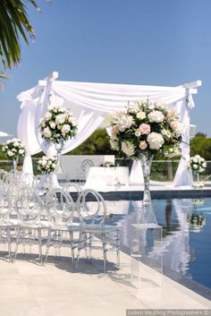 an outdoor wedding set up with chairs and flowers on the side of the pool area