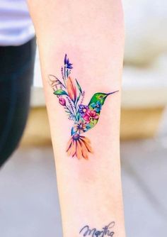 a hummingbird tattoo on the arm with flowers in it's beak and wings