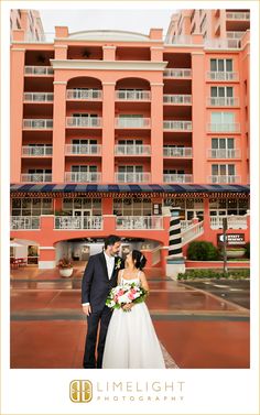 a bride and groom standing in front of an orange building with balconies on it