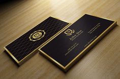 two black and gold business cards sitting on top of a wooden table next to a lamp