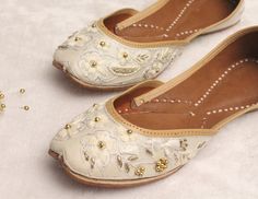 a pair of white shoes sitting on top of a bed next to a beaded flower