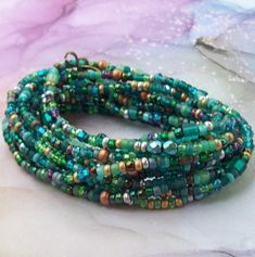 "Gorgeous Peacock. 81\" long, with a golden brass hook infinity clasp. Glass, crystal, satin glass, jade, topaz, Multiple neck wraps and 10 to 12 wrist wraps. Beads are 3mm to 4mm." Faceted Beads Wrap Bracelet For Festivals, Green Hand-strung Jewelry For Festivals, Wrap Bracelet With Faceted Beads For Festivals, Wrap Bracelet With Faceted Round Beads For Festival, Multi-strand Faceted Beads Wrap Bracelet For Jewelry Making, Bohemian Wrap Bracelet With Colorful Beads For Party, Bohemian Party Wrap Bracelet With Colorful Beads, Green Bohemian Wrap Bracelet For Festival, Green Multi-strand Beaded Necklaces For Festivals