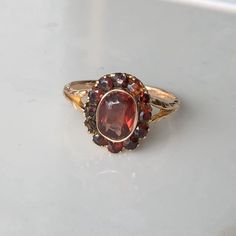 A Vintage 9 carat gold Garnet ring. This beautiful piece holds a gorgeous collection of deep red stones in a gold setting, holding them high up on display. CONDITION: Wear consistent with age and use. Visible glue repair on two small garnet settings. Please see photos for more detail. SETTING SIZE: 12mm x 10mm LARGEST GARNET SIZE: 7mm x 5mm BAND WIDTH: 1mm RING SIZE: UK: M | US: 6 1/4 WEIGHT: 2.0 grams Garnet Ring Engagement, Gold Garnet Ring, Garnet Engagement Ring, Red Stones, Gold Diamond Band, Garnet Jewelry, Garnet Ring, Red Band, Cluster Earrings