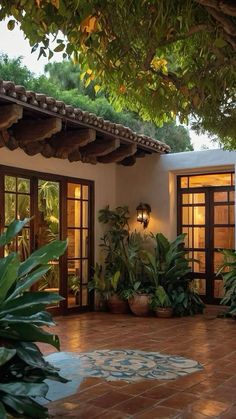 an outdoor patio with potted plants and lights on the side of the house, surrounded by greenery