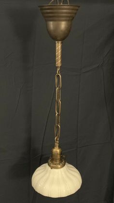 an antique brass chandelier hanging from a chain on a black background with a white glass shade